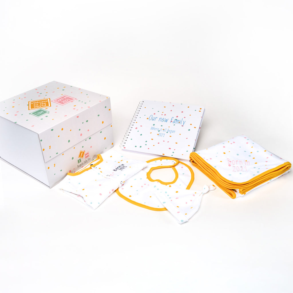 Baby essentials gift box, containing  memory box, memory book, baby blanket, baby grow and bib all with a  neutral dotty pattern with an orange trim that can all be personalised from the Bespoke Baby Box brand