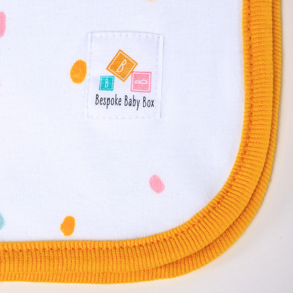 Close up of the Bespoke Baby Box logo label on a baby Blanket in neutral pastel colours with an orange trim.