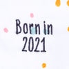 Close up of the words "Born in 2021" in grey thread embroidered on a Baby grow with neutral dotty pattern design with orange trim.