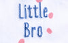 Close up of the words "Little Bro" in blue thread embroidered on a Baby grow with neutral dotty pattern design with orange trim.